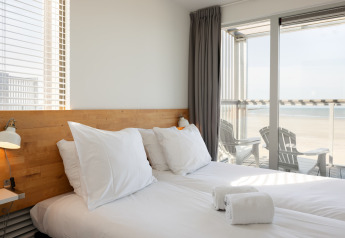 Dormitorio luminoso con cama doble, almohadas grandes y vista al mar en Resort Hoek van Holland, Países Bajos.