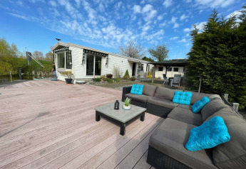 Ampio patio in legno con divano ad angolo grigio e cuscini blu alla Villa «Avondrood» nei Paesi Bassi.