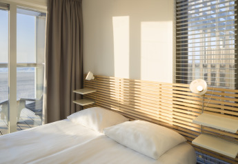 Dormitorio en una casa de playa en Resort Hoek van Holland, Países Bajos, con sol y vistas al mar desde la ventana.