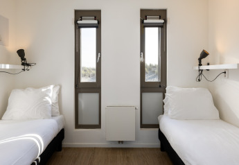 Dos camas individuales en una habitación luminosa con ventanas altas en el Resort Hoek van Holland en los Países Bajos.
