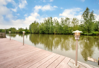 Vista dal terrazzo in legno con lampade sul fiume calmo e alberi presso Villa Avondrood nei Paesi Bassi.