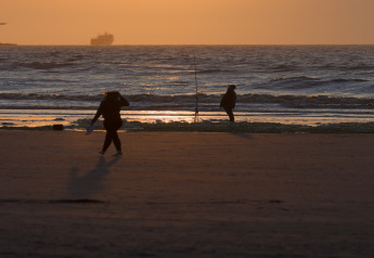 Siluetas de personas en la playa al atardecer en Resort Hoek van Holland, Países Bajos, con un barco en el horizonte.