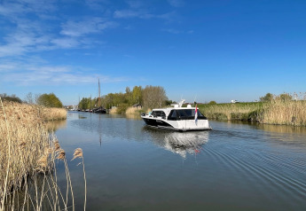 Vista di un canale tranquillo con barche e canne presso Villa Avondrood nei Paesi Bassi sotto cielo sereno.
