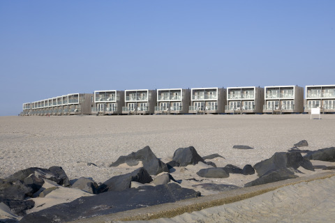 Moderne Strandhäuser im Resort Hoek van Holland, Niederlande, mit Sand und Felsen im Vordergrund.