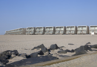 Moderne Strandhäuser im Resort Hoek van Holland, Niederlande, mit Sand und Felsen im Vordergrund.