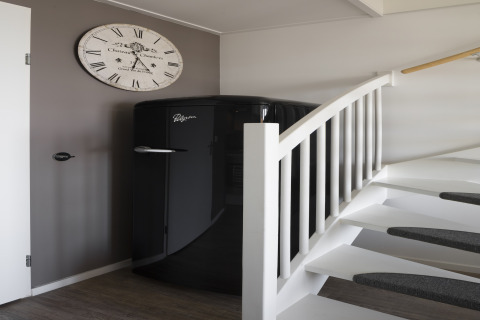 Schwarzer Kühlschrank und weiße Treppe im Strandhaus Resort Hoek van Holland, Niederlande, mit Uhr.
