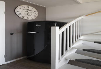 Nevera negra y escalera blanca en casa de playa del Resort Hoek van Holland, Países Bajos, con gran reloj de pared.