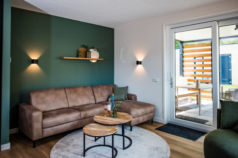 Soggiorno di lodge moderno con divano marrone, parete verde, tavolini rotondi e accesso al patio esterno.