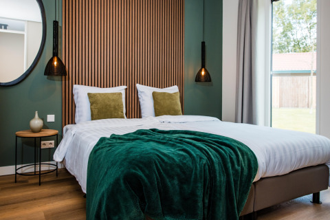 Hyggeligt værelse i lodge med dobbeltseng, grøn plaid, moderne belysning og store vinduer.