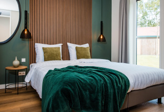 Camera da lodge accogliente con letto doppio, plaid verde, luci moderne e grande finestra.