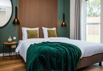Hyggeligt værelse i lodge med dobbeltseng, grøn plaid, moderne belysning og store vinduer.
