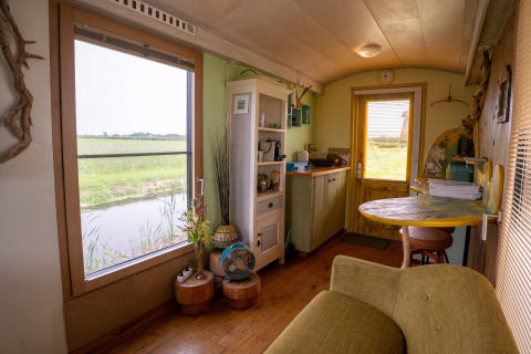 Sala y cocina de una casa pequeña con vista a campos y agua cerca de la costa en los Países Bajos.