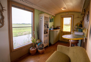 Wohnbereich und Küche eines Tiny House mit Blick auf Felder und Wasser nahe der Küste in den Niederlanden.