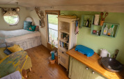 Sfeervol tiny house in Nederland met bed, ronde raamopening, houten vloer en compacte keuken.