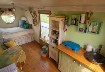 Gezellige tiny house in Nederland met bed, ronde raampartij, houten vloer en kleine keuken.
