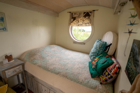 Gemütliches Schlafzimmer in einem Tiny House in den Niederlanden mit rundem Fenster und Tagesdecke.
