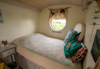 Acogedora habitación en una tiny house en Países Bajos, con ventana redonda y colcha estampada.