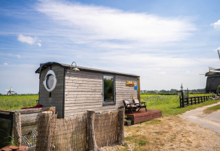 Kleines Holzhaus in den Niederlanden neben einem Feld, Windmühlen und blauem Himmel im Hintergrund.