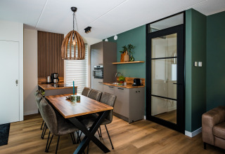 Cucina e zona pranzo lodge moderna con pareti verdi, dettagli in legno, porta in vetro e arredo elegante.
