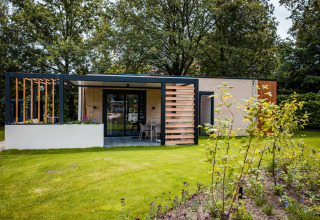 Modernes Lodge mit Terrasse und großem Garten, umgeben von Bäumen und Blumenbeeten im Grünen.