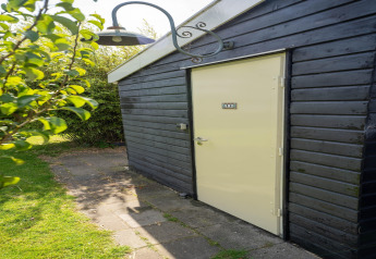 Ingangsdeur van een tiny house in Nederland met zwarte houten gevel en tuinpad in het zonlicht.