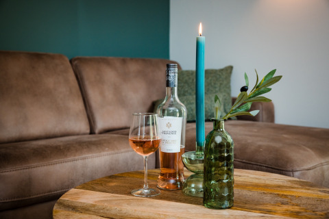 Et hyggeligt stuebord i en lodge med rosévin, glas, grøn vase med gren og tændt blå lysestage.