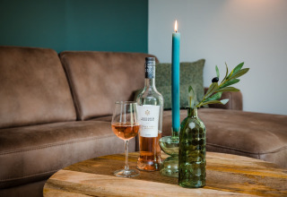Gezellig tafeltje in een lodge met roséwijn, glas, groene vaas met takje en blauwe kaars.