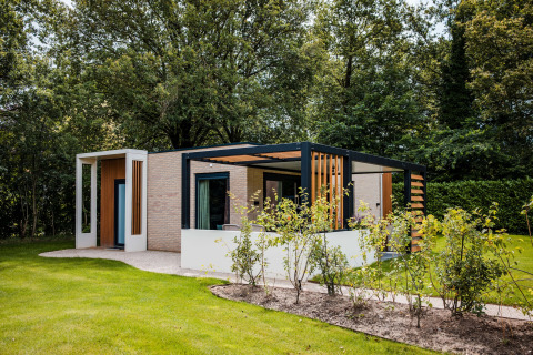 Moderne lodge met open terras in een groene omgeving, omgeven door bomen en netjes onderhouden gras.