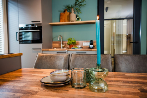 Cocina de lodge moderna con mesa de madera, platos de cerámica, vasos y vela azul sobre portavelas.
