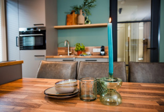 Hedendaagse lodgekeuken met gedekte houten tafel, keramiek, glazen en een brandende blauwe kaars.
