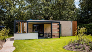 Lodge moderno con terrazza e giardino, circondato da alberi e fiori, ideale per rilassarsi nella natura.