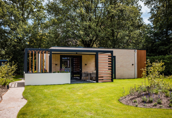 Moderne lodge met terras en groene tuin, omgeven door bomen en bloemen, ideaal om te ontspannen.
