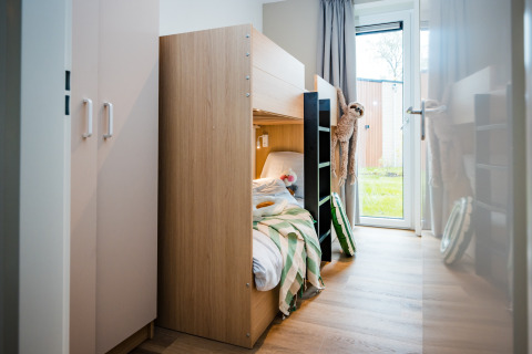 Camera di lodge moderna con letto a castello in legno, piumone a righe verdi, peluche e vista sul giardino.