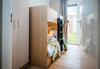 Moderne lodgeværelse med køjeseng, grønstribet dyne, tøjdyr og udsigt til haven gennem glasdør.