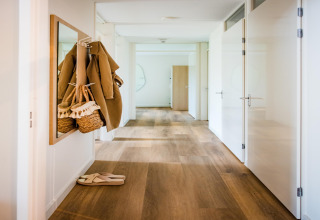Corridoio luminoso in un lodge, pavimento in legno, cappotto e borsa vicino a uno specchio, ciabatte.