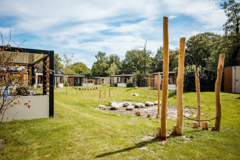 Udsigt over et hyggeligt lodgeområde med moderne hytter, grønne græsplæner og legeplads i træ.