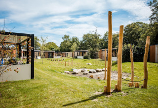 Lodgegebied met moderne chalets, groene grasvelden en een houten speelplek in het midden van het terrein.