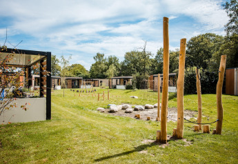 Udsigt over et hyggeligt lodgeområde med moderne hytter, grønne græsplæner og legeplads i træ.
