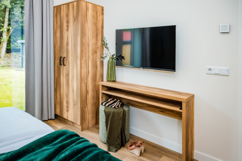 Modernes Lodge-Zimmer mit Holzschrank, Wand-TV, Gründecke und Blick auf den Garten durch das Fenster.