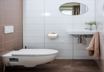 Moderne lodge-badeværelse med væghængt toilet, håndvask, spejl og beige håndklæde ved siden af.