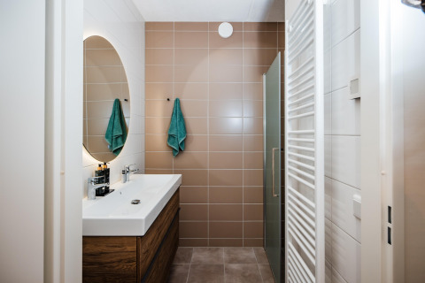 Bagno moderno in un lodge con piastrelle marroni, lavabo bianco, mobile in legno e asciugamani verdi.