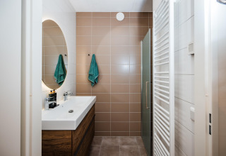 Bagno moderno in un lodge con piastrelle marroni, lavabo bianco, mobile in legno e asciugamani verdi.
