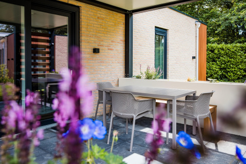 Udendørs terrasse ved en lodge med moderne møbler, blomster i forgrunden og lyse murstensvægge.