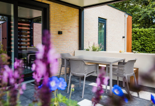 Patio moderno in una lodge con tavolo da pranzo all'aperto, sedie, fiori in primo piano e mura di mattoni.