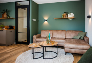 Moderne lodge-stue med grøn væg, beige hjørnesofa, sofaborde og dekoreret hylde over sofaen.