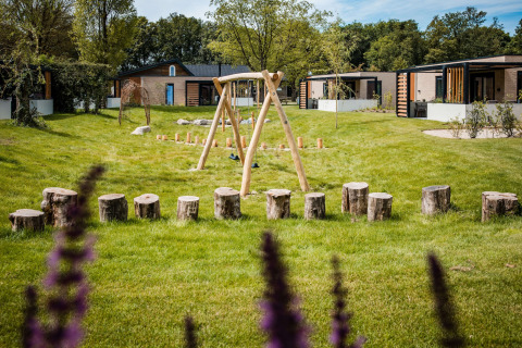 Natuurlijke speeltuin met houten schommels en boomstammen bij moderne lodges te midden van het groen.