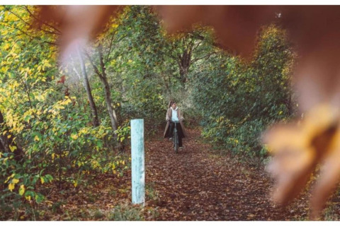 Person fährt Fahrrad auf einem herbstlichen Waldweg, umgeben von Bäumen, nahe einer Lodge aufgenommen.
