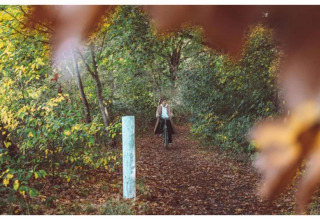 Persoon fietst op een bospaadje in de herfst, foto gemaakt aan een lodge omgeven door bomen.