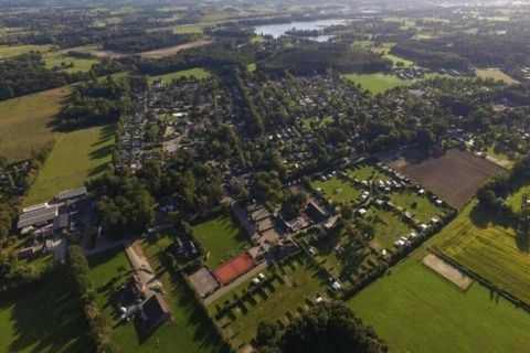 Luftfoto af et lodgeområde med grønne marker, bygninger og træer under en lys himmel i landskabet.