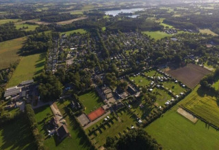 Luchtzicht op een lodge met groene grasvelden, gebouwen, bomen en landelijke omgeving in de zon.